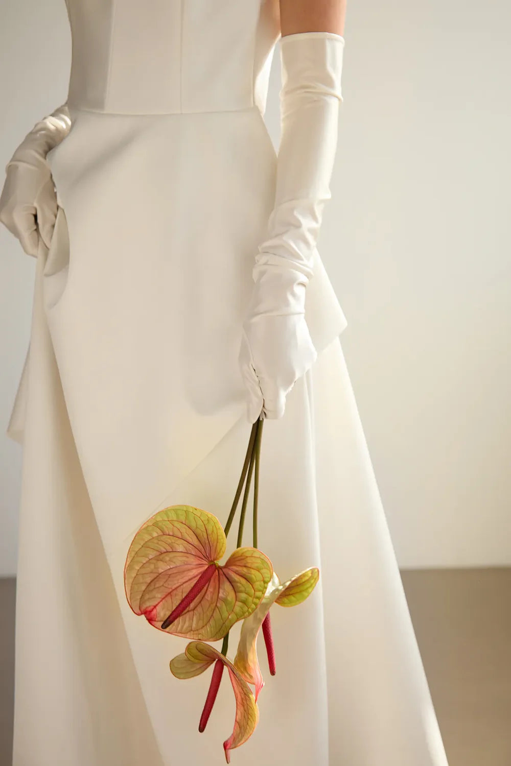 woman wearing extra long snug and tight wedding gloves matching her wedding gown. She holds a flower in her hand